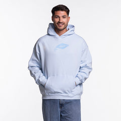 A man stands facing forward, smiling with hands in the pocket of a light blue Court Culture Original Vice Nights "Drive-In" Oversized Unisex Hoodie, featuring a small chest graphic. He pairs it with blue jeans against a white background.